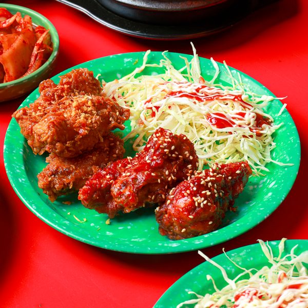 ไก่ทอดกรอบและไก่ทอดซอสโรยงาบนจานสีเขียว เสิร์ฟกับกะหล่ำปลีฝอยราดซอส มีกิมจิอยู่ด้านข้าง