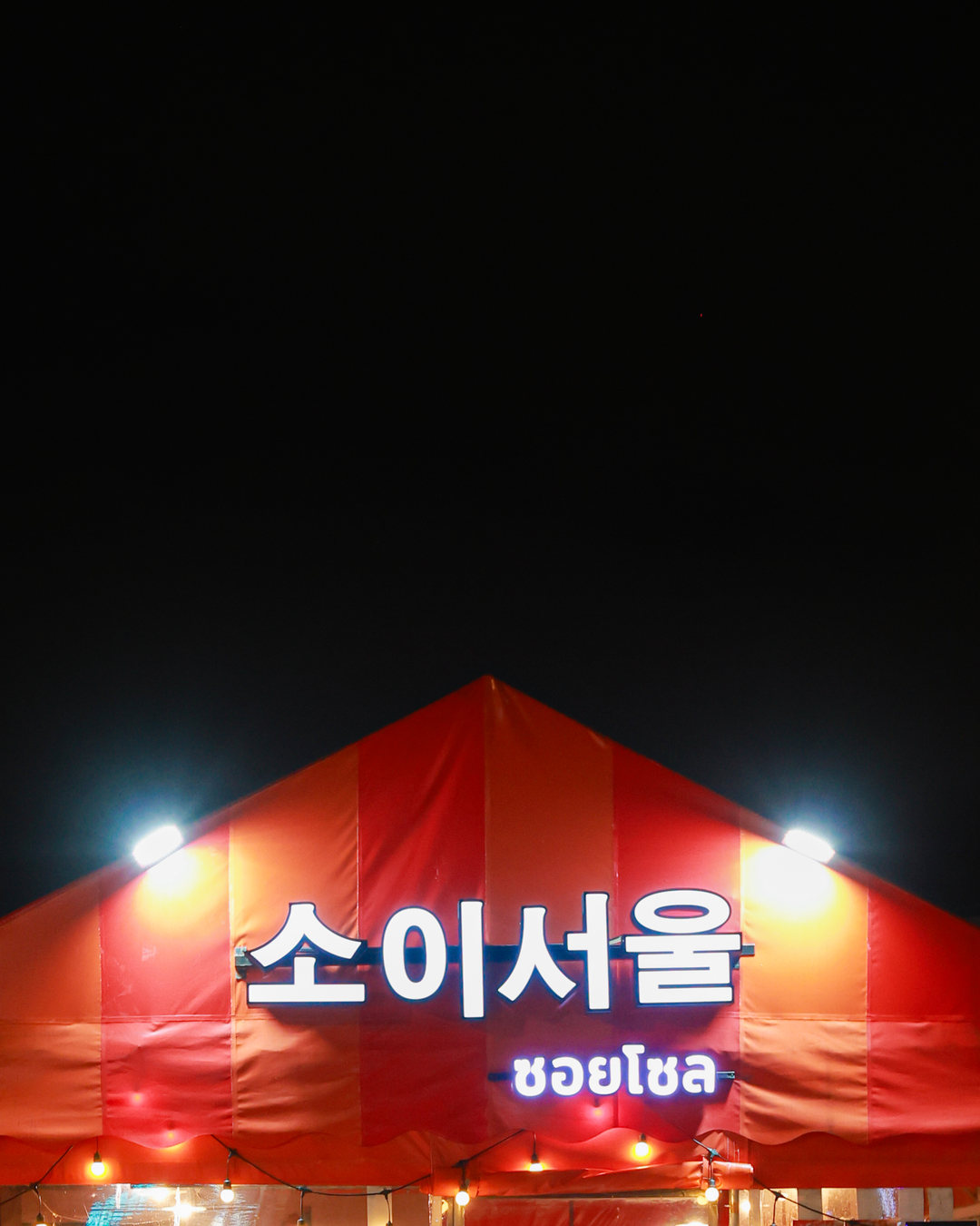 เต็นท์ส้มของร้านซอยโซล สาขาช้างคลาน ยามค่ำคืน ป้ายไฟ 소이서울 · ซอยโซล กับหลอดไฟระย้าใต้ชายคา