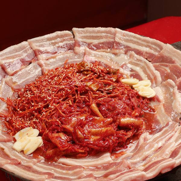 หมูสามชั้นวางเรียงรอบกระทะ ตรงกลางเป็นกิมจิและเห็ดเข็มทองคลุกซอสแดงโรยงา พร้อมกระเทียม